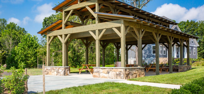 wooden pavilion sitting beneath blue sky and in front of newly built home and tree line