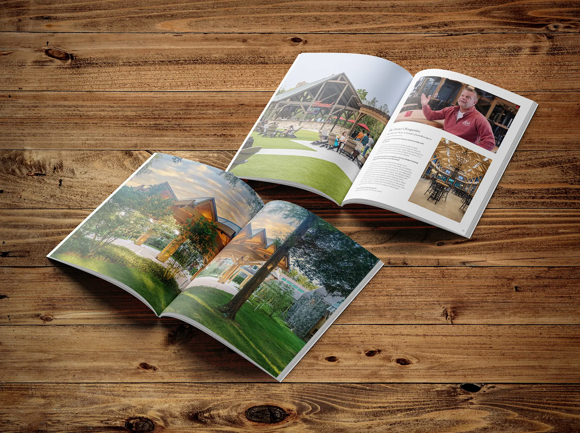 Two open magazines with photos of buildings, green outdoor spaces, and a person are displayed on a wooden surface, creating a captivating timber frame project gallery.