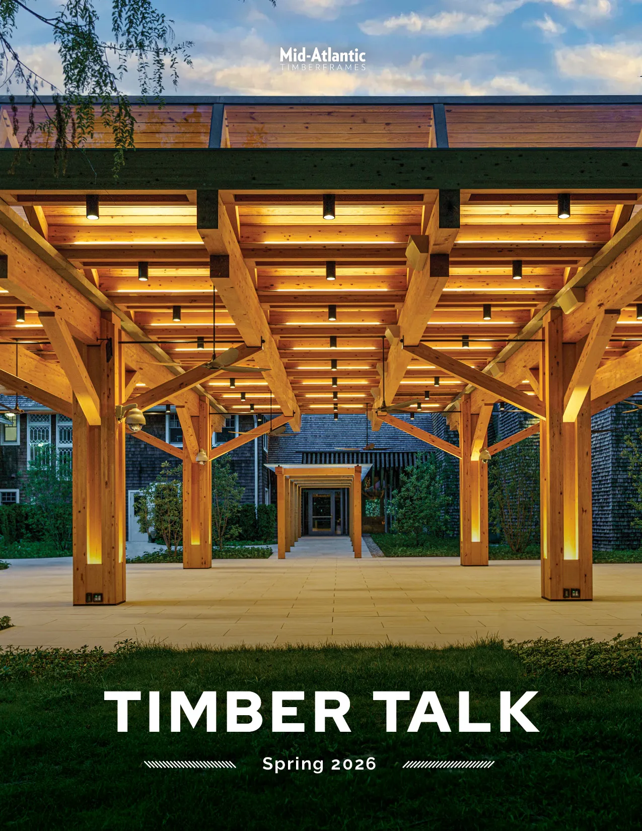 Cover of “Timber Talk” magazine featuring a view through a well-lit exterior timber pavilion, framed the sky at dusk above and grass in front of the pavilion below. Header reads Mid-Atlantic Timberframes. Issue is Spring 2026.
